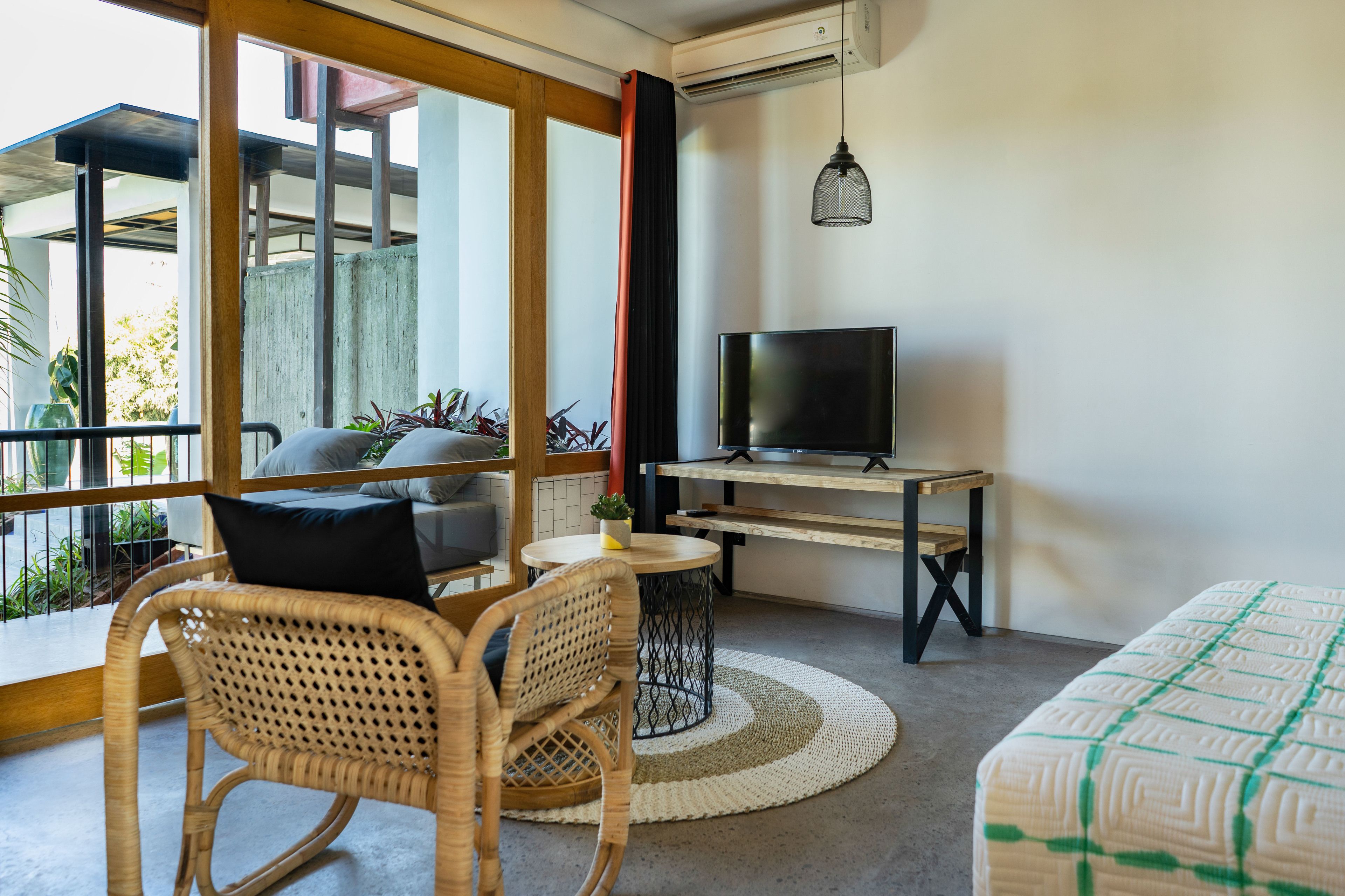A modern living room with a sofa, a TV on a wooden table, wicker chairs, and a view of the outdoors.