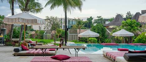 Un espace aménagé au bord de la piscine, avec des chaises longues et des parasols, entouré de palmiers et donnant sur une piscine.
