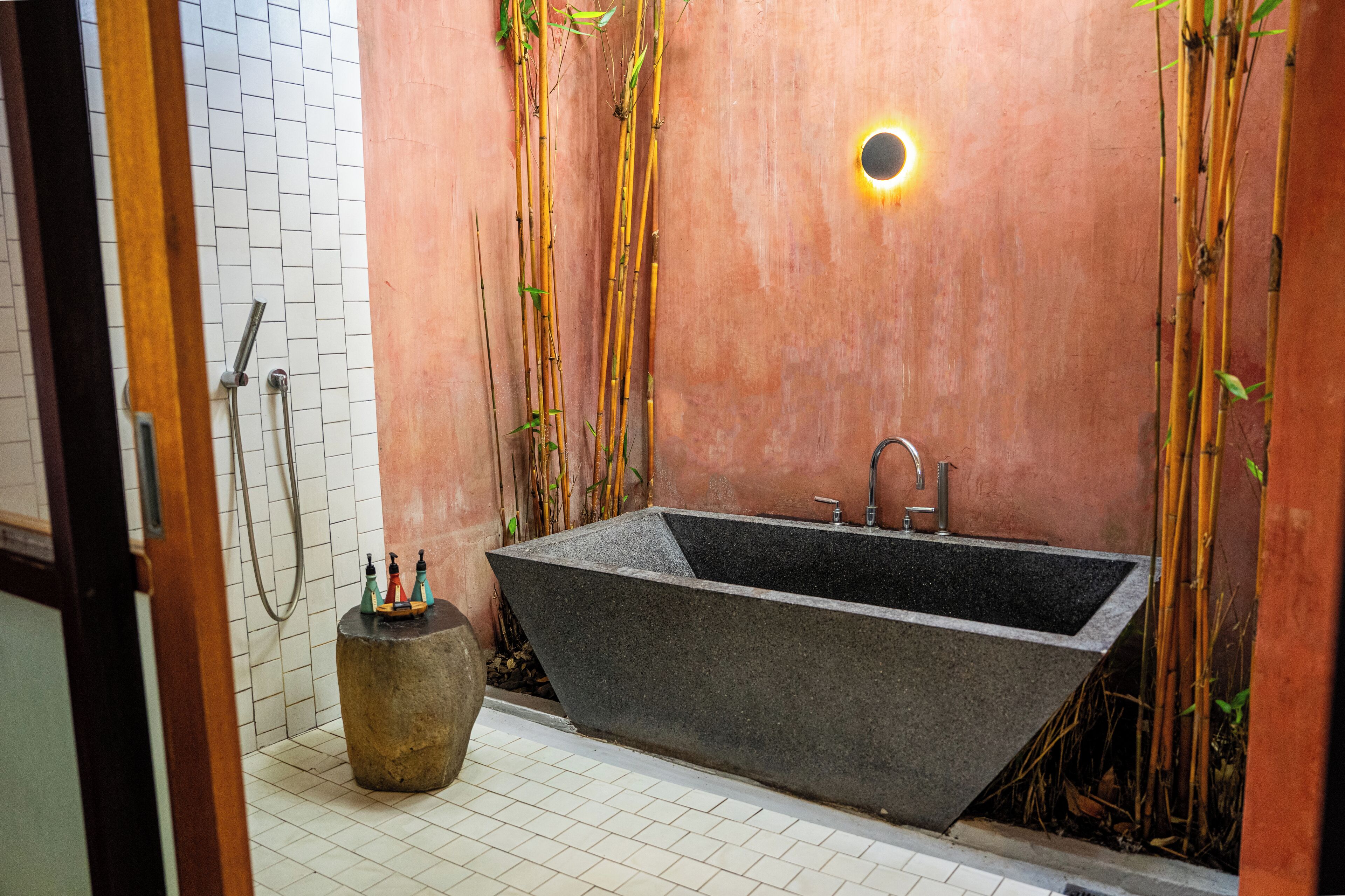 A modern bathroom with a freestanding bathtub, bamboo decor, and a small round table with bottles.