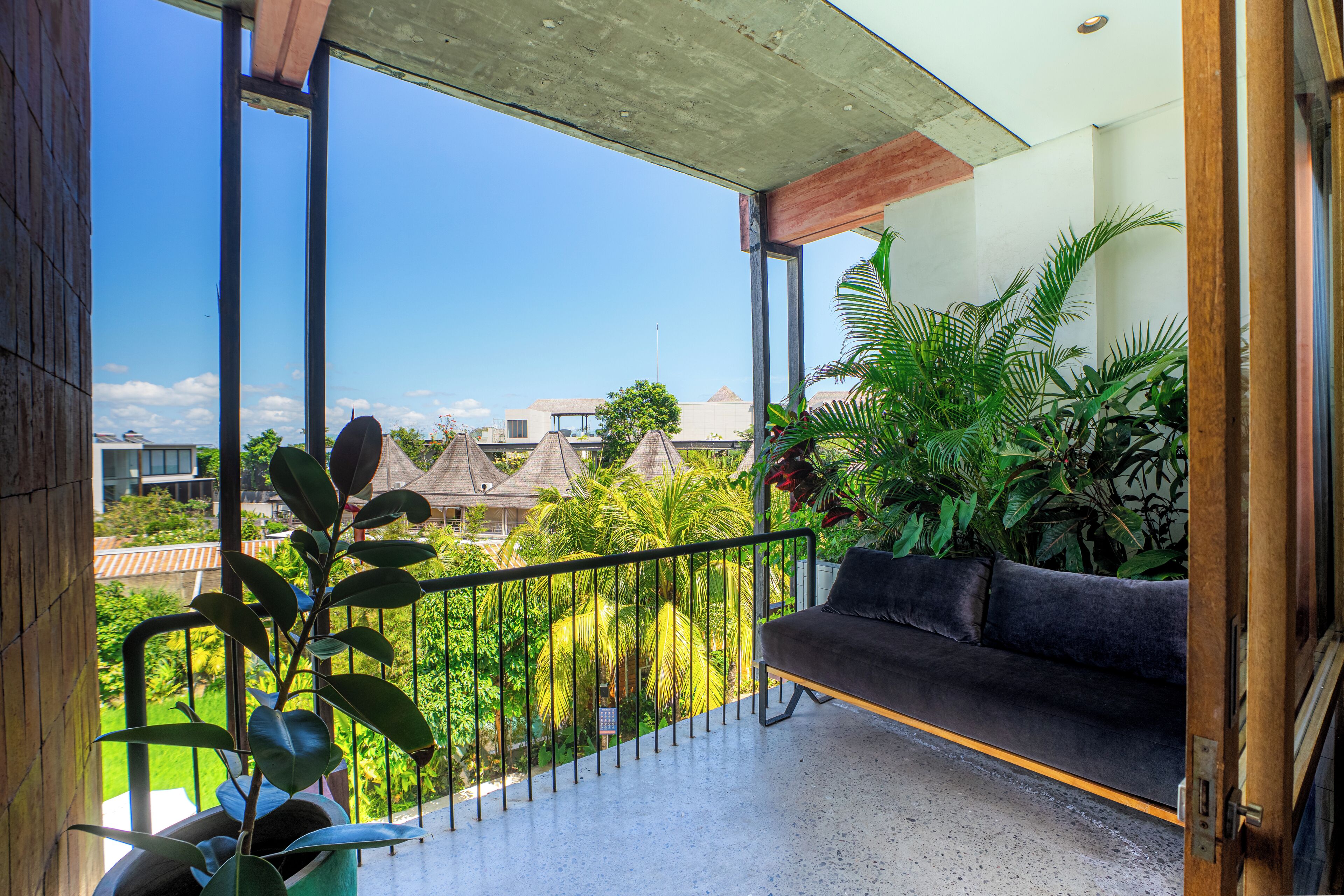 A balcony with a sofa, potted plants, and a view of buildings and trees.