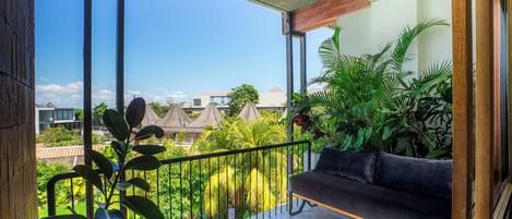 A balcony with a sofa, potted plants, and a view of buildings and trees.
