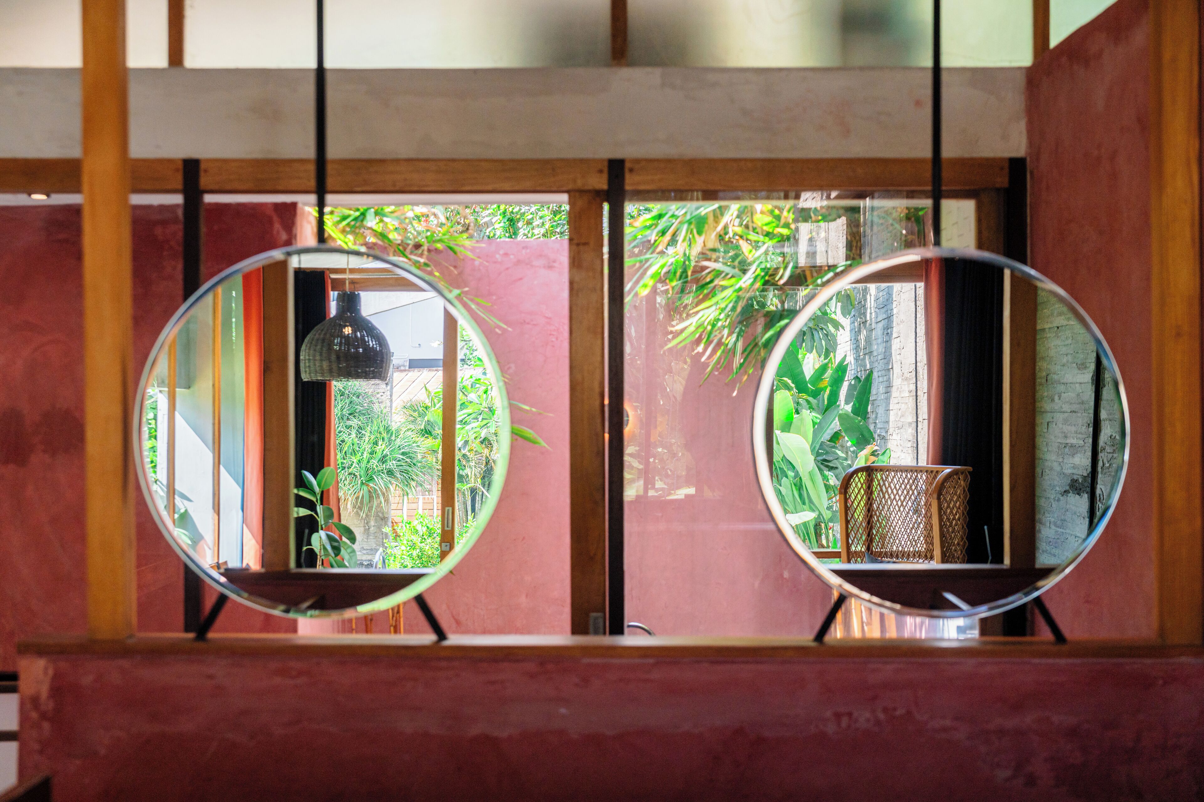 Two round mirrors on stands, reflecting a room with a red wall, a window, and a chair.