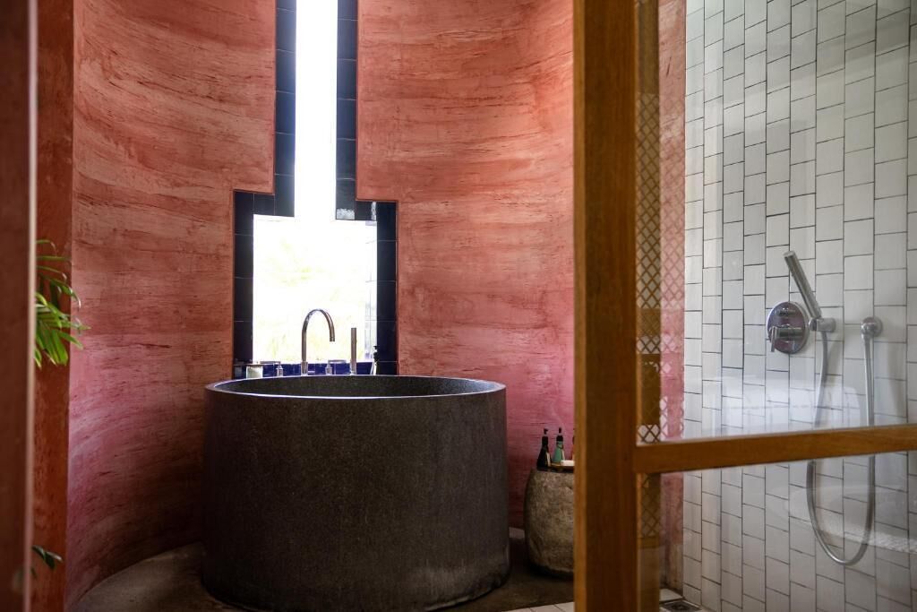 A bathroom with a large, round sink, a window, and a shower area.