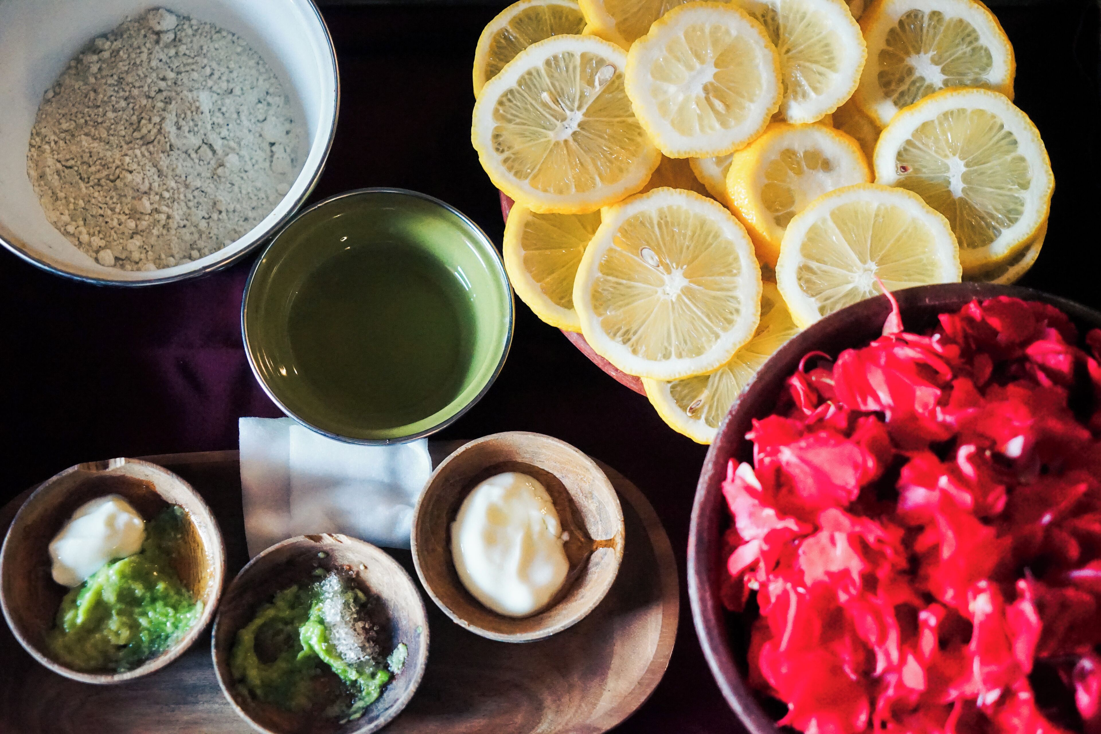 Un tavolo con diversi cibi tra cui ciotole di guacamole, fette di limone e un vaso di fiori rossi.