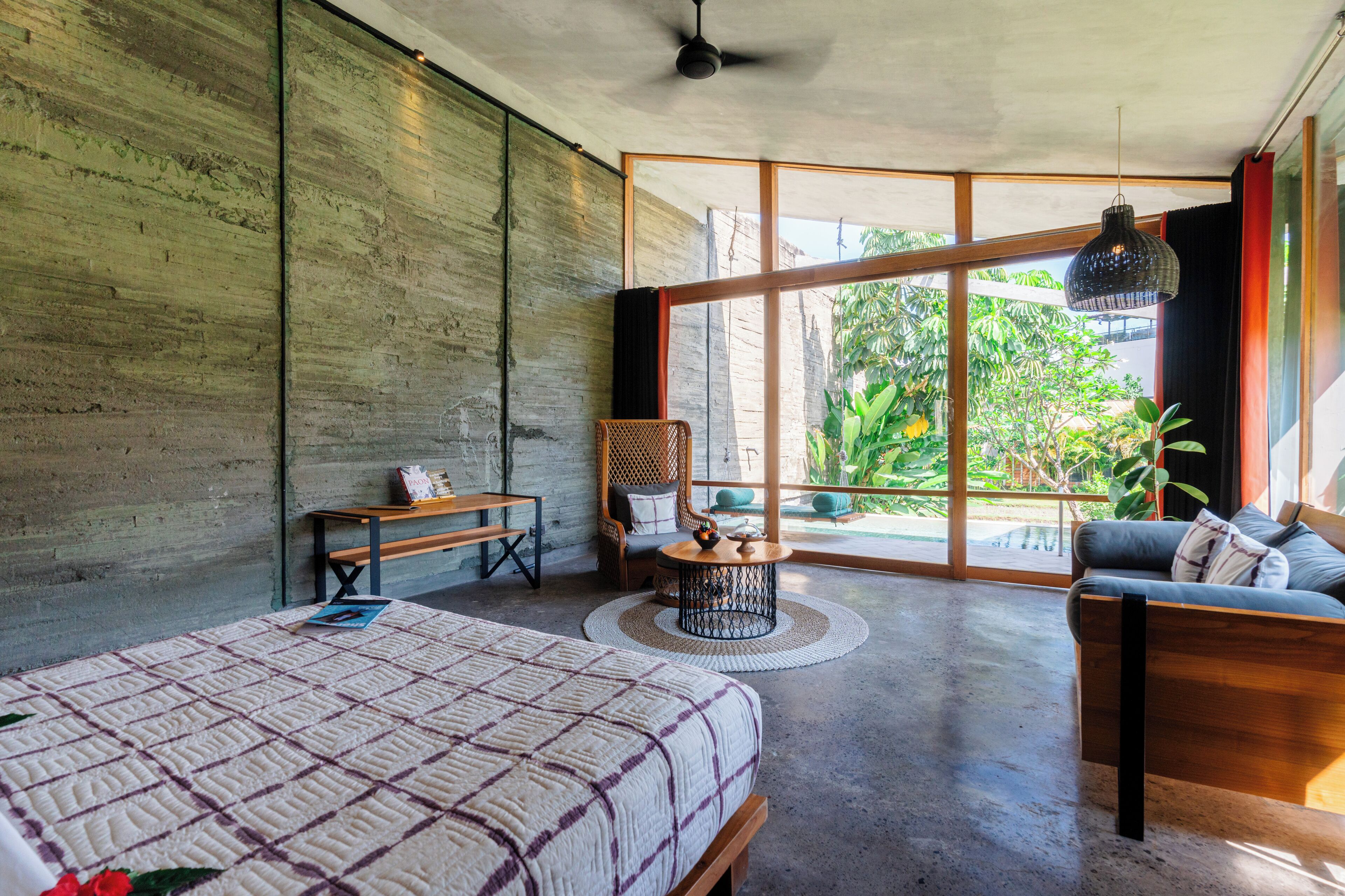 Une chambre moderne avec un grand lit, un canapé, une petite table et une chaise. Une grande fenêtre offre une vue sur la verdure à l’extérieur.
