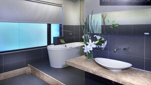 Un baño moderno con bañera, lavabo e inodoro. Hay una ventana que ofrece vistas al cielo y una planta en la encimera.