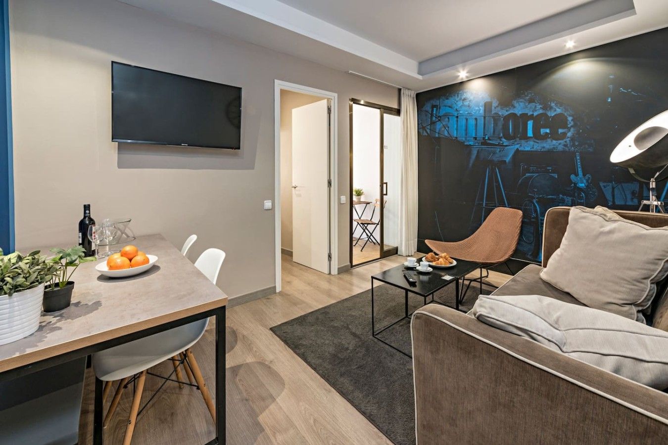 En moderne stue med et fladskærms-tv, et spiseområde med bord og stole, en sofa og en vægmonteret lampe.