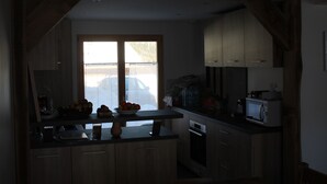 A kitchen with wooden cabinets, a microwave, and a window with a view of a car outside. - Chalet adjoining Les Contamines-Montjoie, sleeps 10 (Les Contamines-Montjoie)