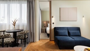 A hotel room with a dark blue sofa, a round table with patterned chairs, a small side table with a vase, and a bed with a headboard. - master Mirabell (Salzburg)