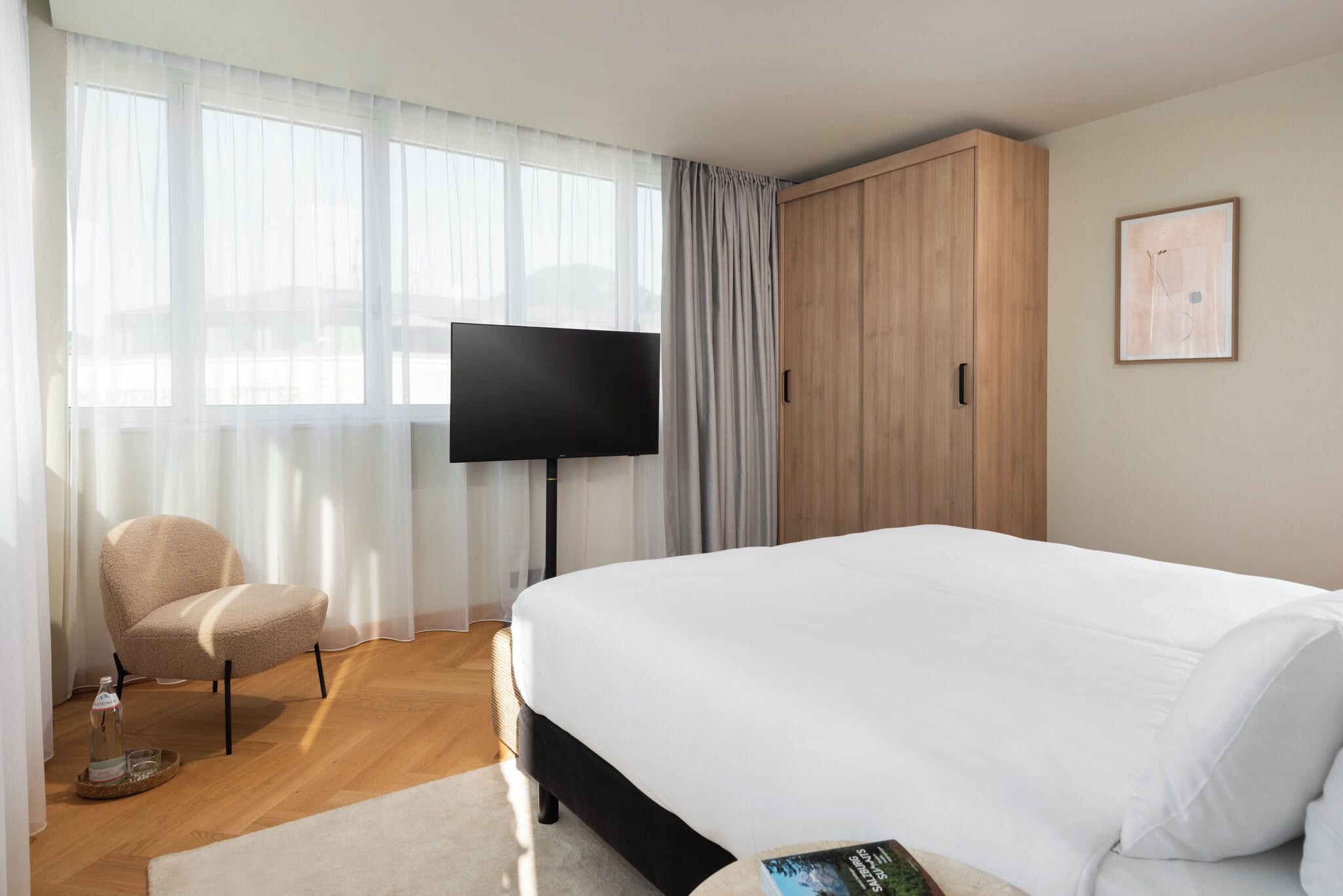 Een hotelkamer met een groot bed, een televisie, een houten garderobe en een stoel.