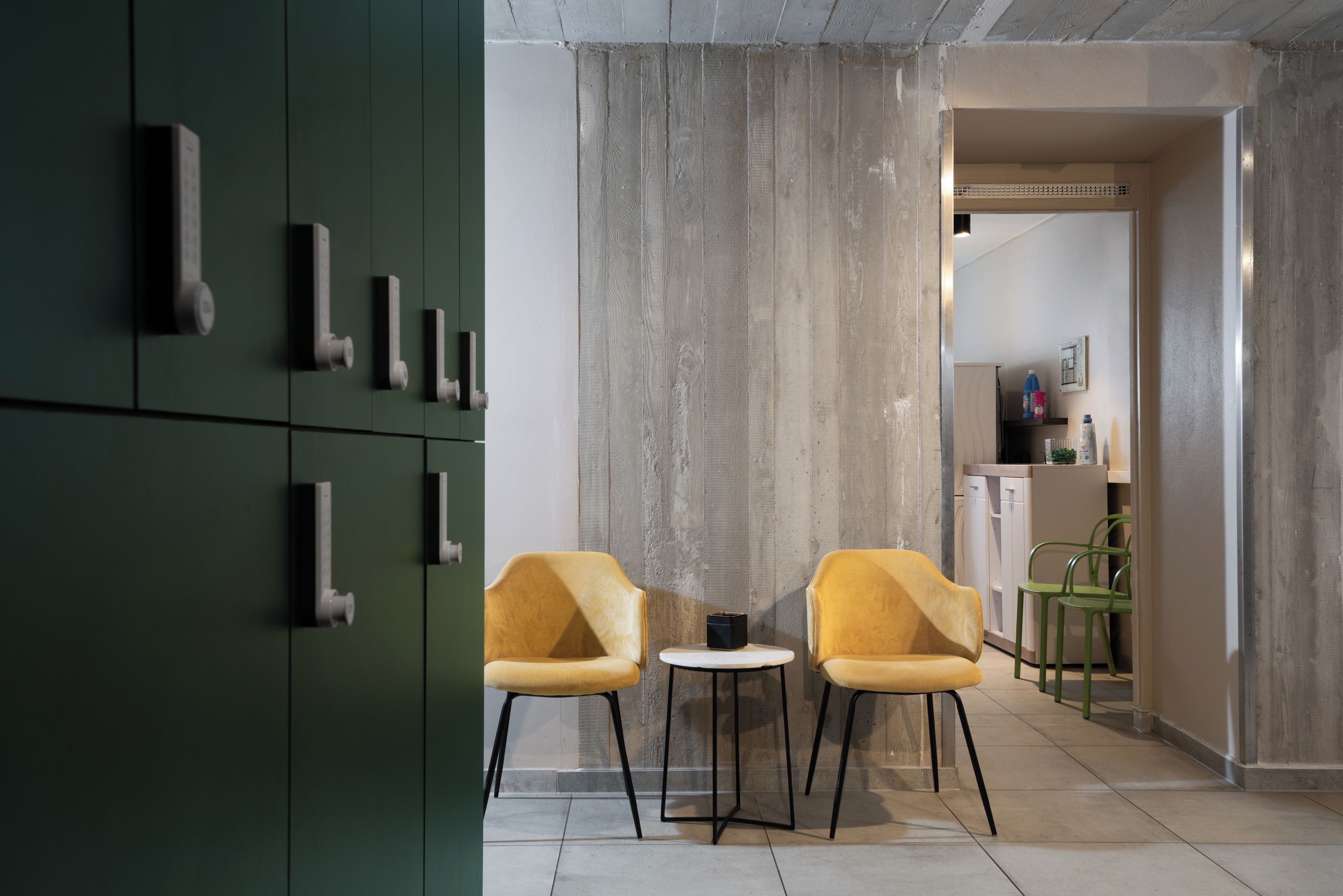 A modern interior with two yellow chairs, a small round table, and a green cabinet with multiple handles.
