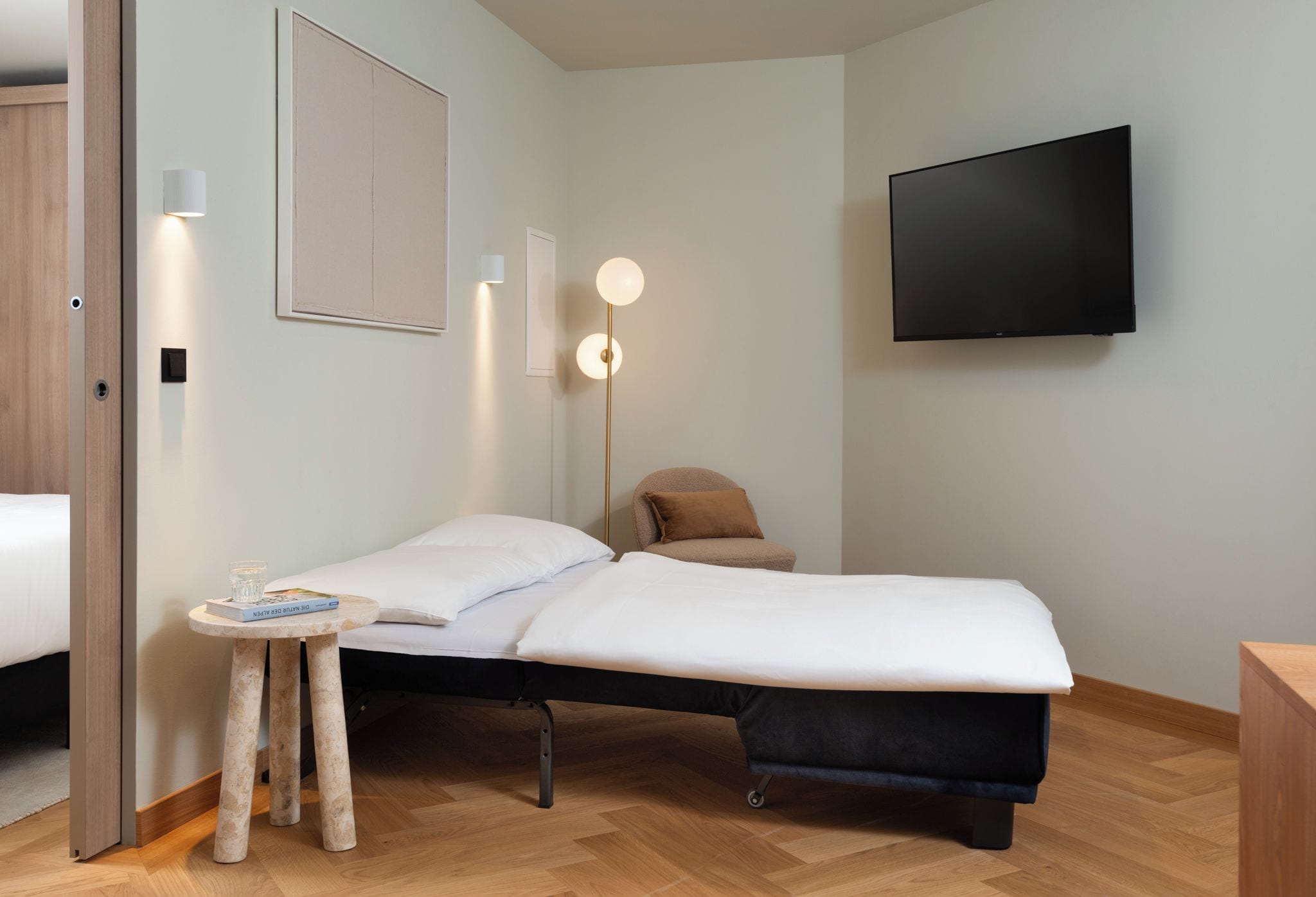 Una camera da letto moderna con un letto singolo, comodino, lampada e televisione a parete.