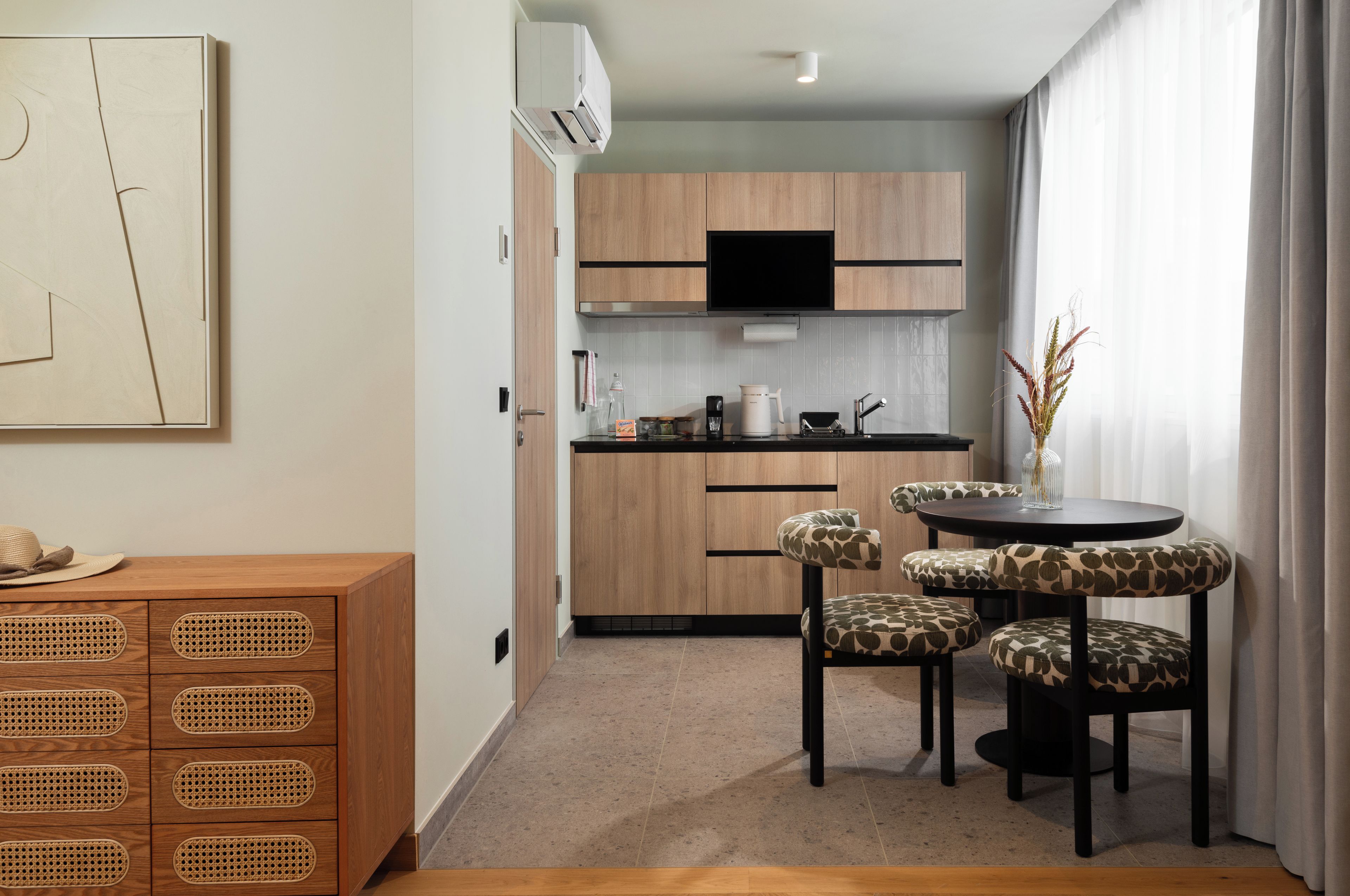A modern kitchen with wooden cabinets, a black TV, and a dining area with four chairs.