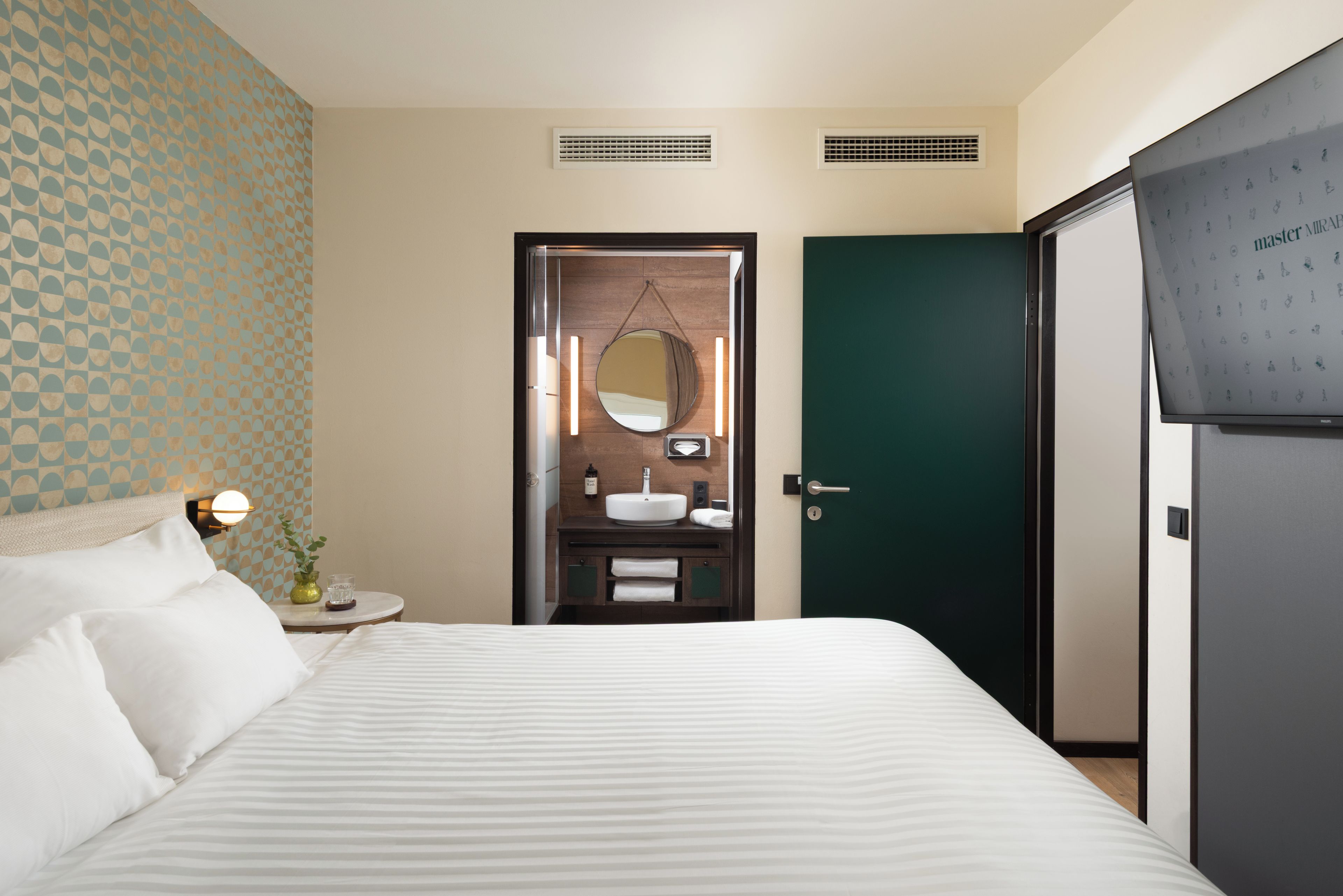 A hotel room with a bed, a bathroom with a sink and mirror, and a green door.