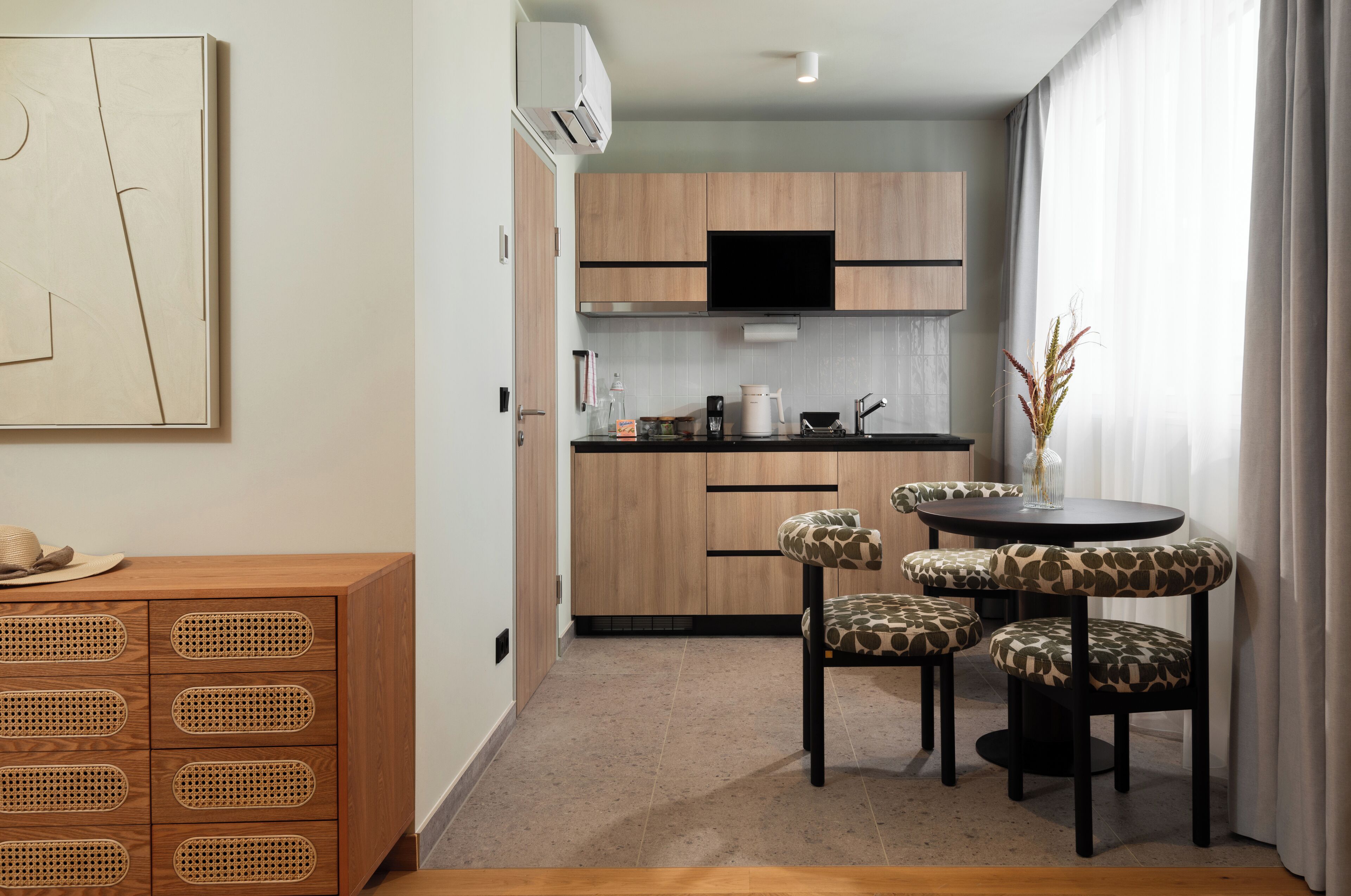 A modern kitchen with wooden cabinets, a black TV, and a dining area with four chairs.