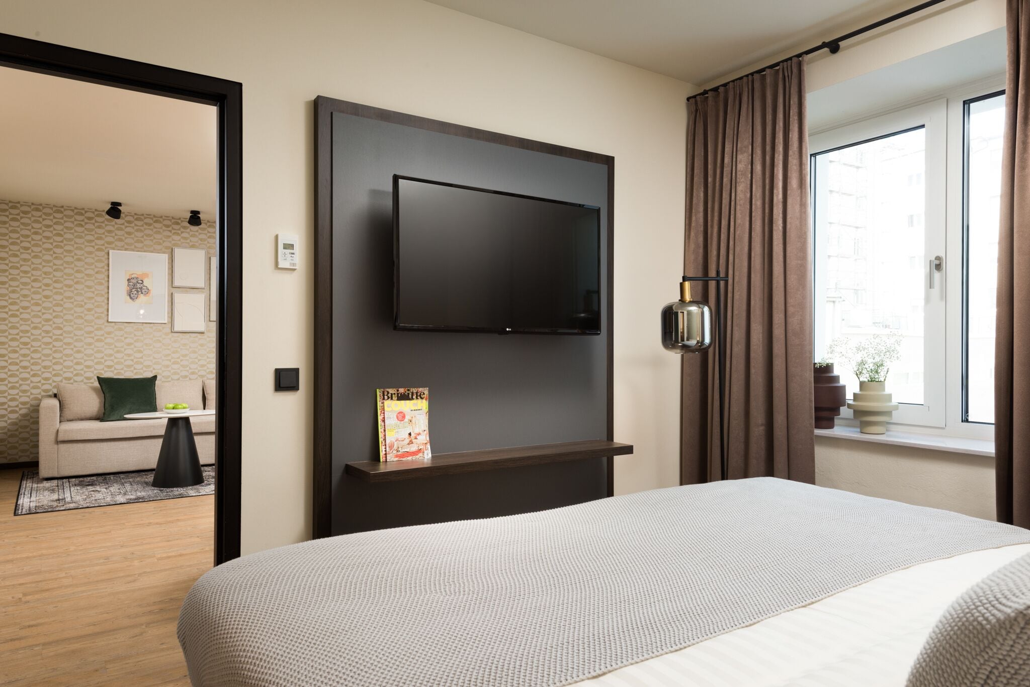 Une chambre d’hôtel comprenant un lit, un téléviseur fixé au mur, une table de chevet, une fenêtre avec des rideaux et une vue sur l’extérieur.