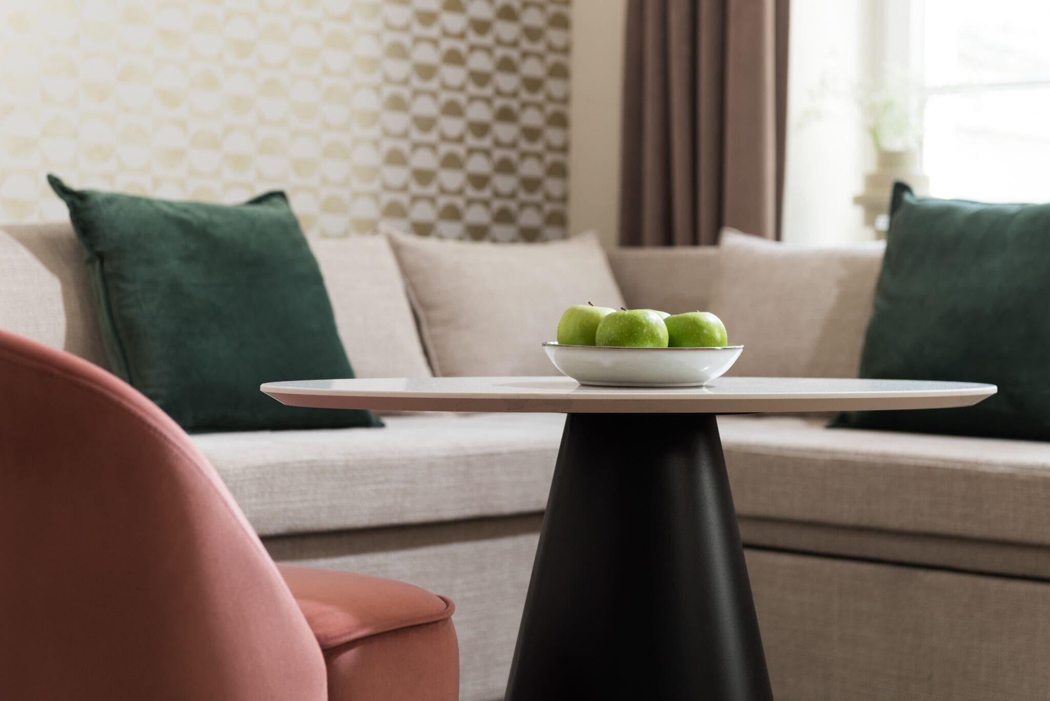 Een moderne woonkamer met een ronde tafel, een schaal groene appels en een bank met groene kussens.