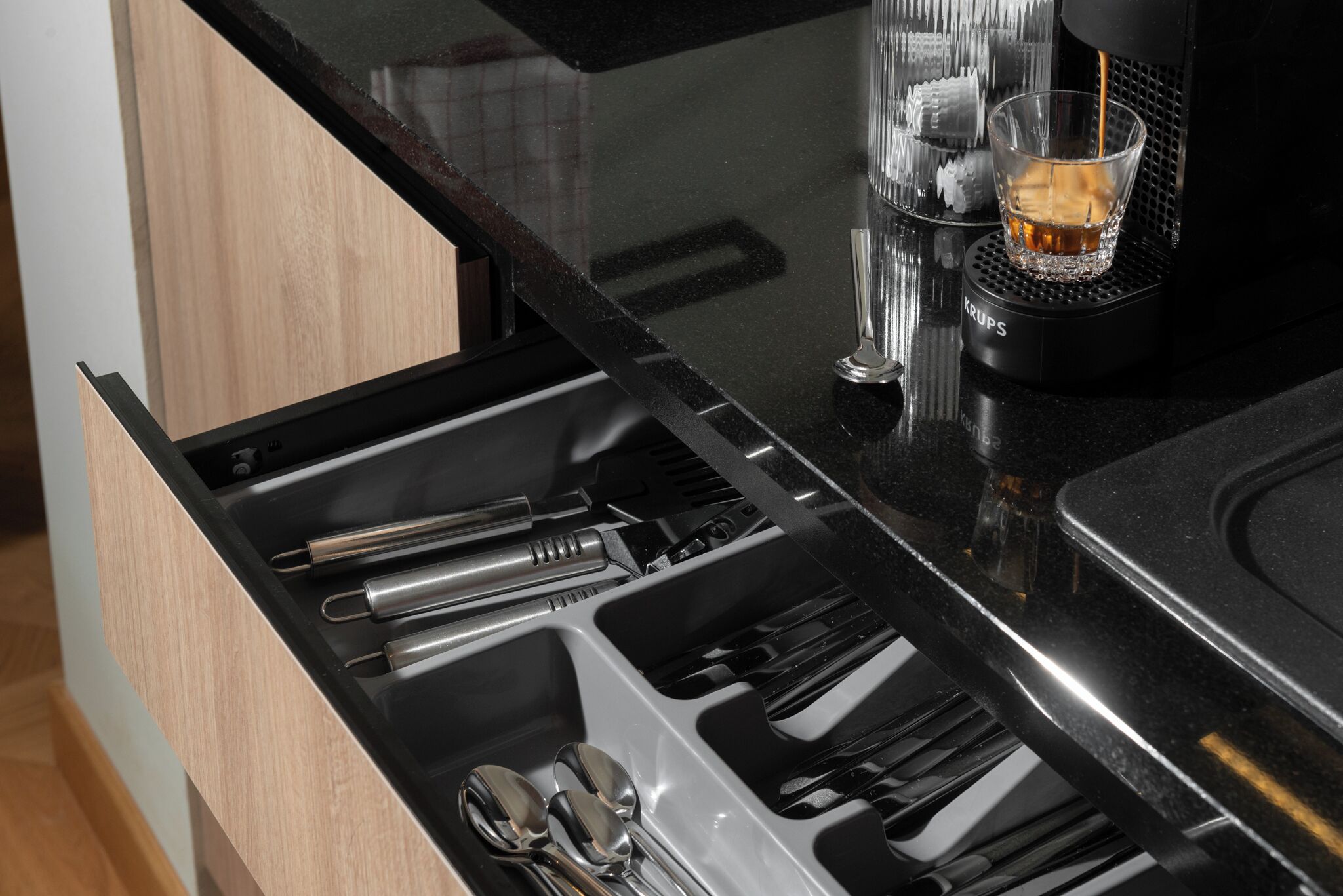 A kitchen with a black countertop, a coffee machine, and a drawer with utensils.