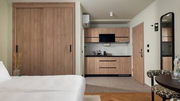 A modern hotel room with a large bed, a small kitchenette, a dining area with a table and chairs, and a large mirror.