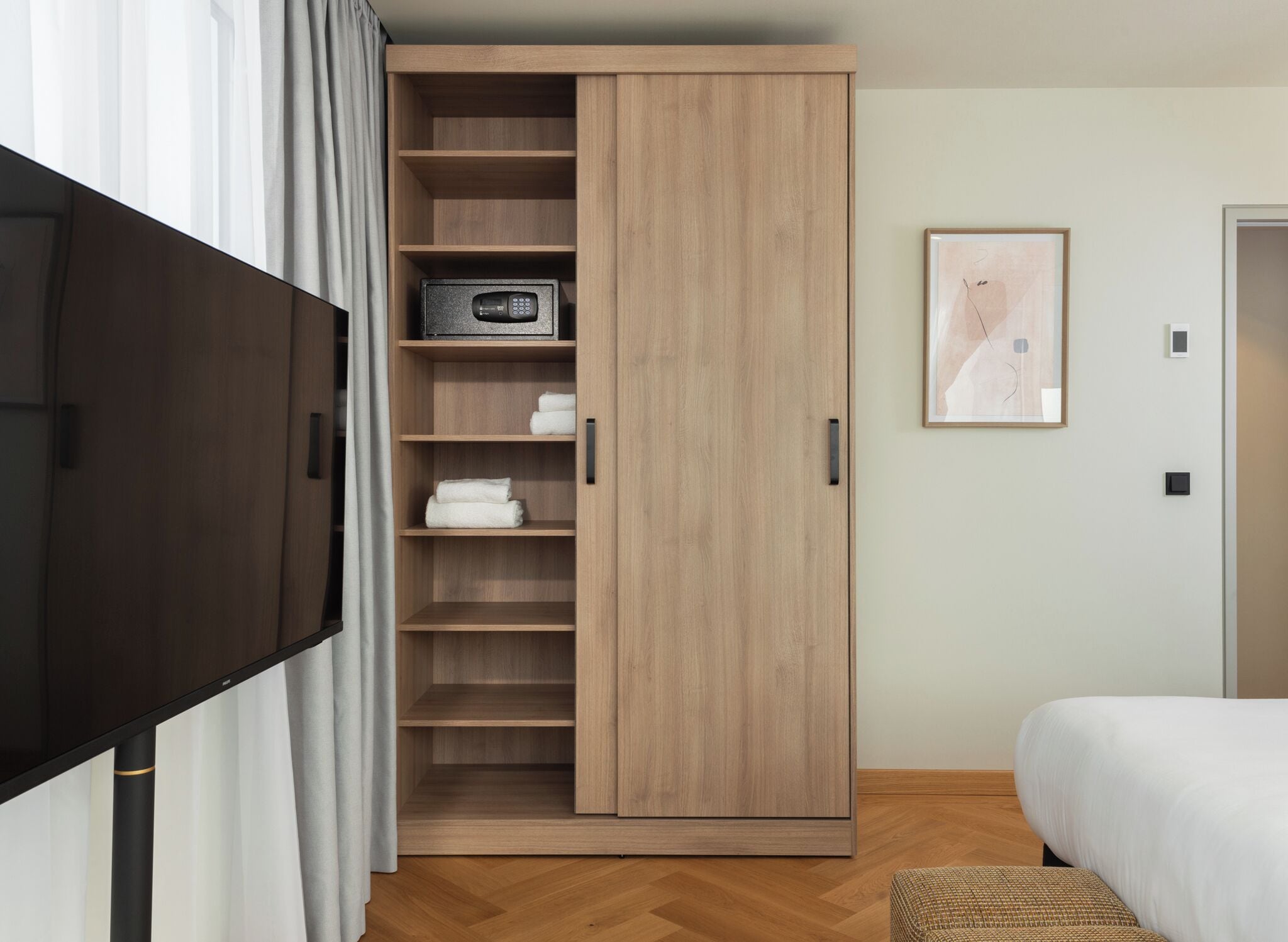 Un dormitorio con cama, televisión, armario y un cuadro en la pared.