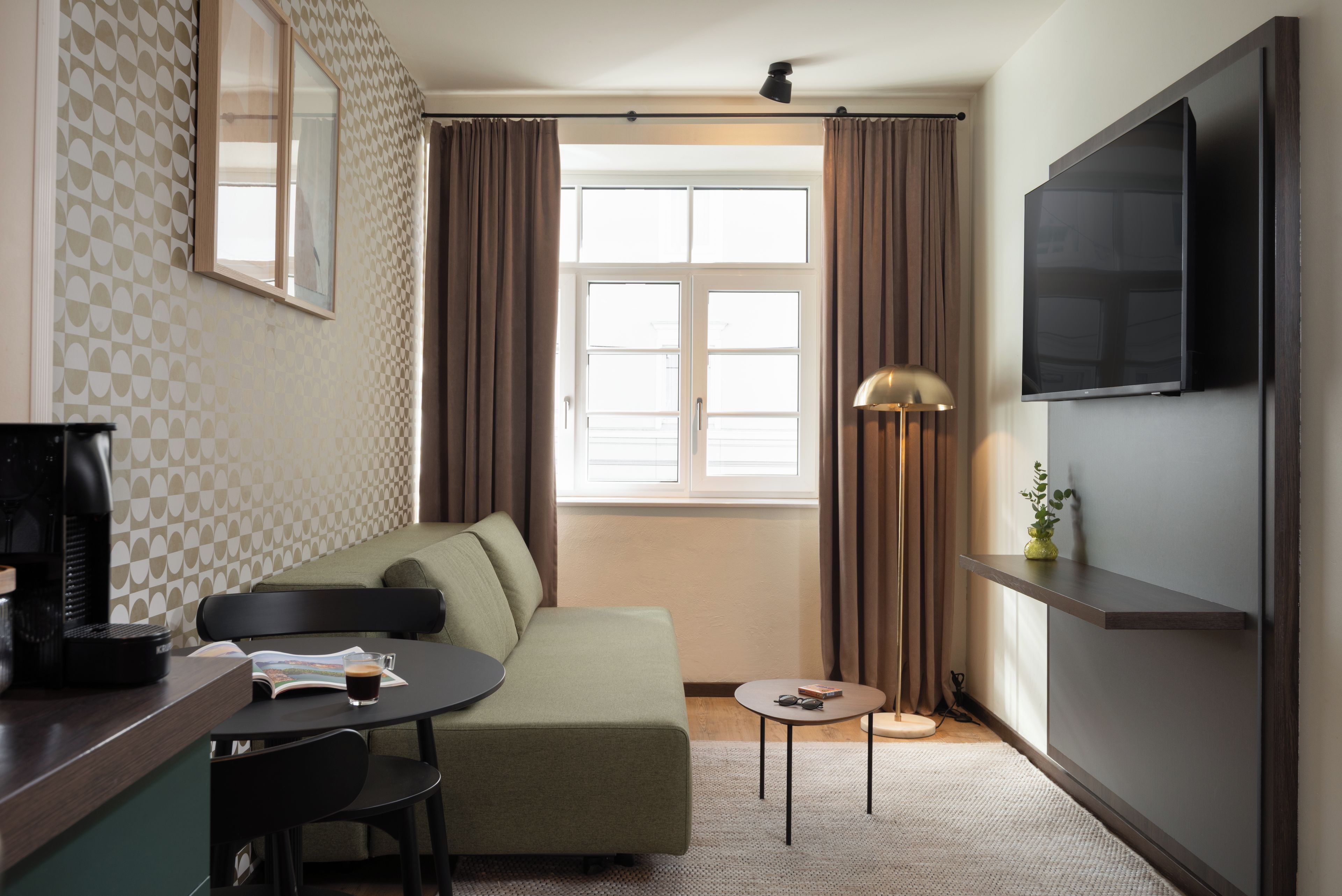 A modern living room with a sofa, a coffee table, a TV mounted on the wall, and a window with curtains.