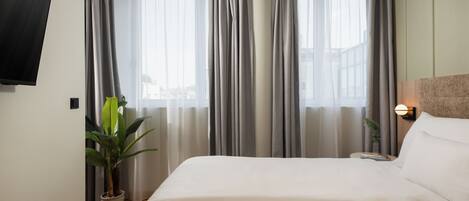 A hotel room with a large bed, a flat-screen TV mounted on the wall, and a potted plant.