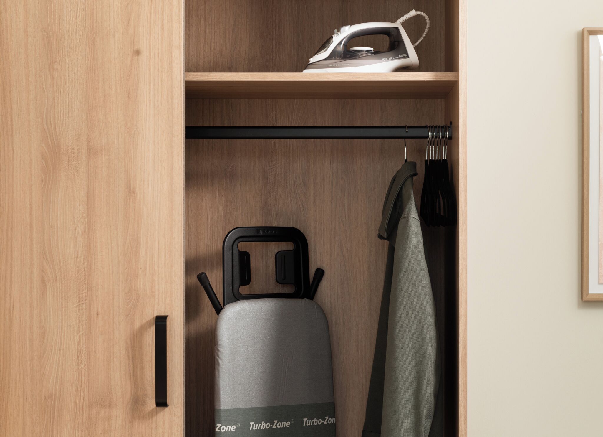 Een garderobe met een kledingroede, een Philips-strijkijzer en een Turbo-Zone apparaat.