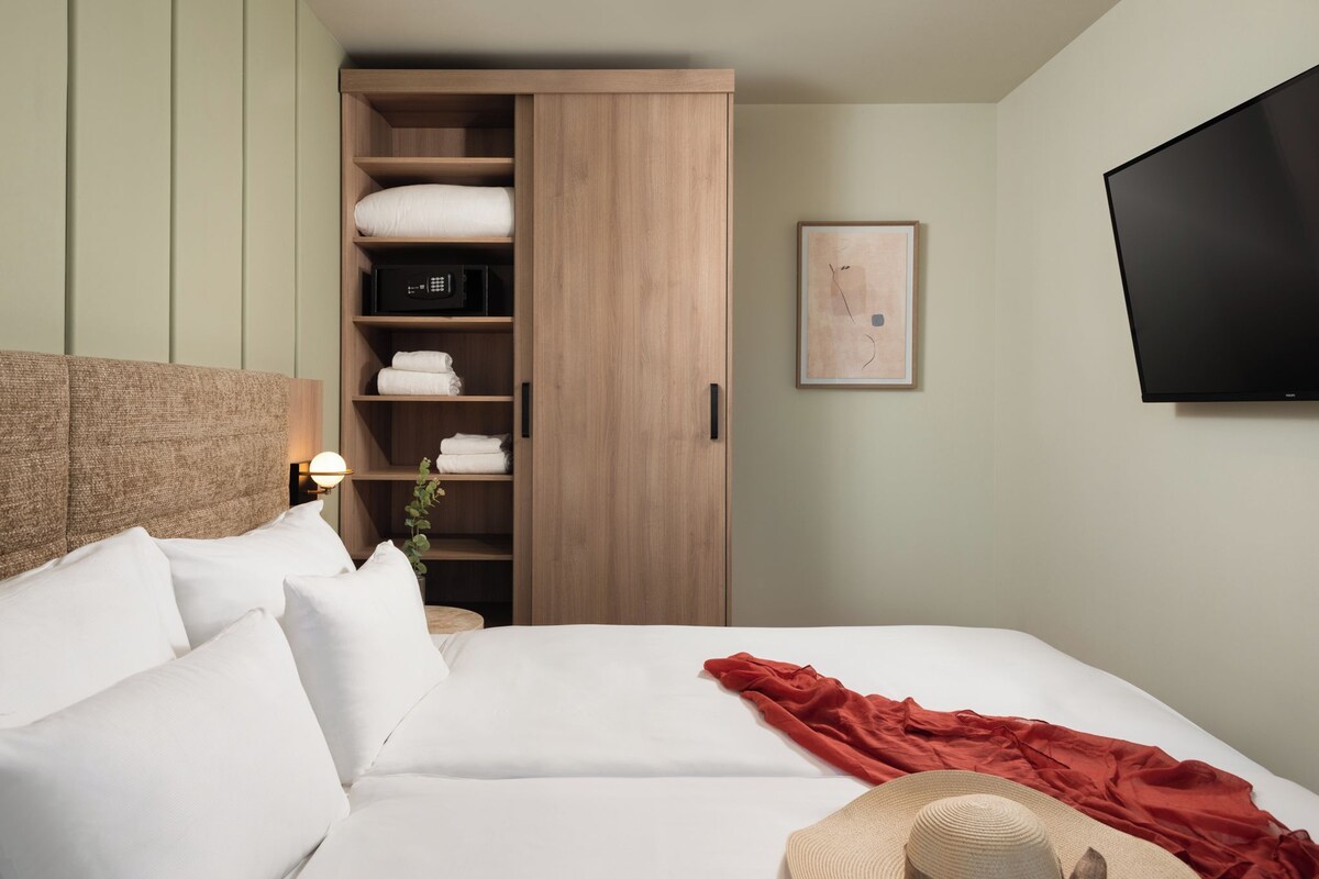 Ein Hotelzimmer mit Bett, Kleiderschrank, Fernseher und einem gerahmten Bild an der Wand.