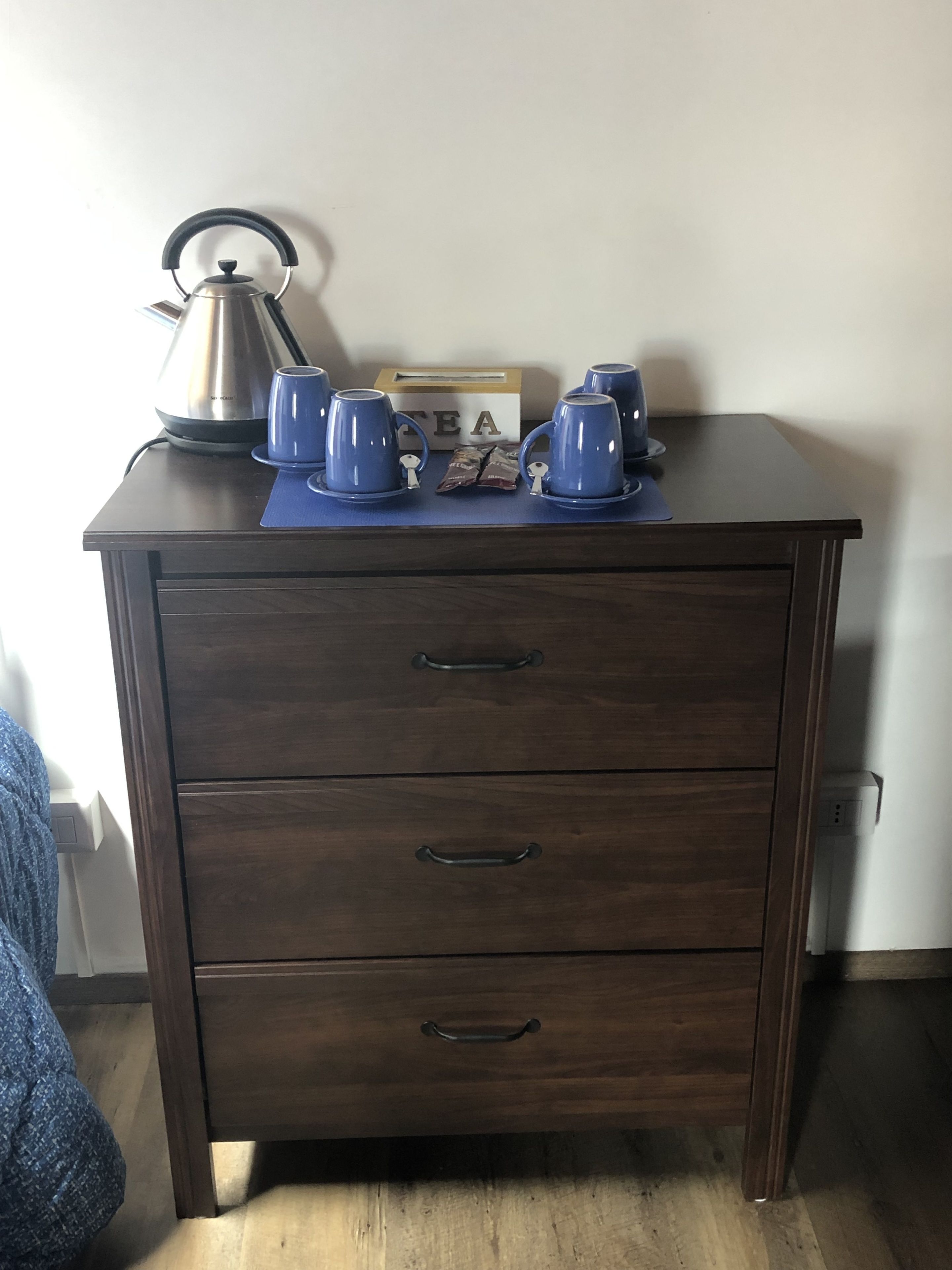 A dark wooden nightstand with three drawers and a kettle on top.