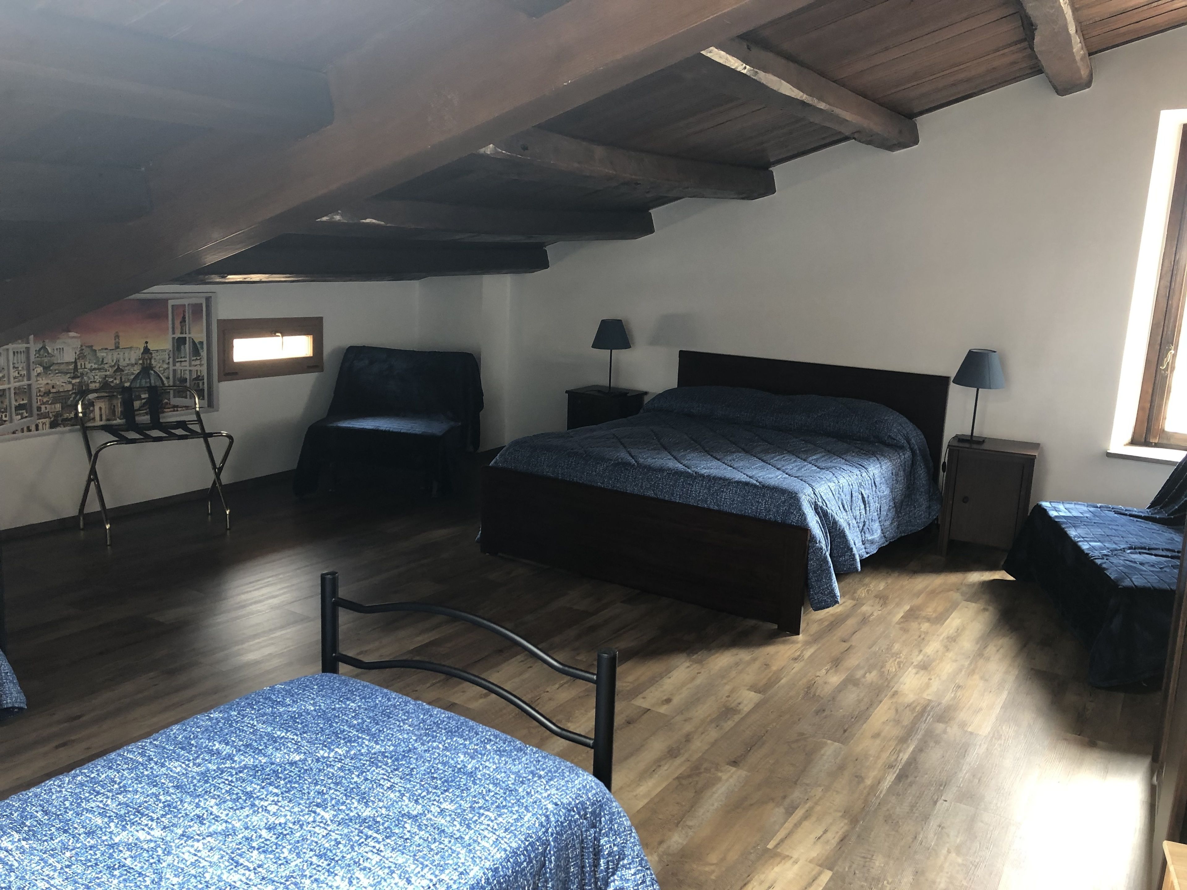 A bedroom with a wooden ceiling, a bed, a chair, a nightstand, and a window.