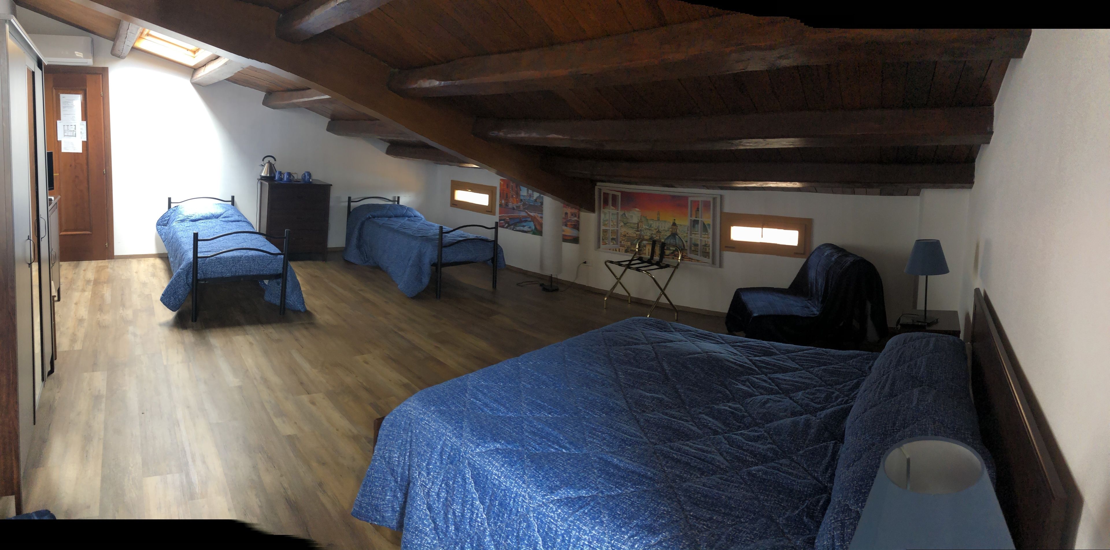A bedroom with two beds, wooden flooring, a ceiling with exposed beams, a desk, and a chair.
