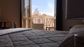 A hotel room with a large bed, a view of the cityscape through a window, and a balcony with a railing. - BB Il Re Alla Reginella Guest House (Rome)