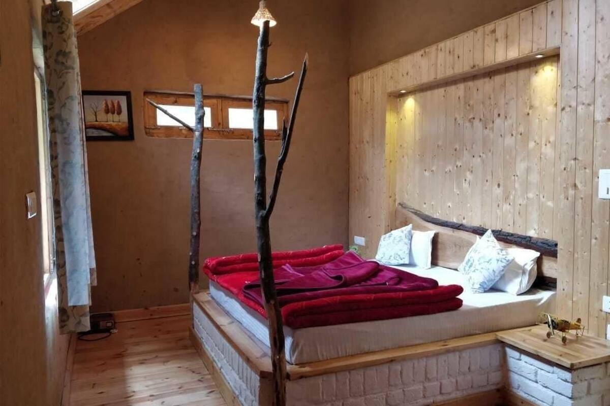 A room with a wooden bed, a red blanket, a wooden headboard, and a small bedside table.