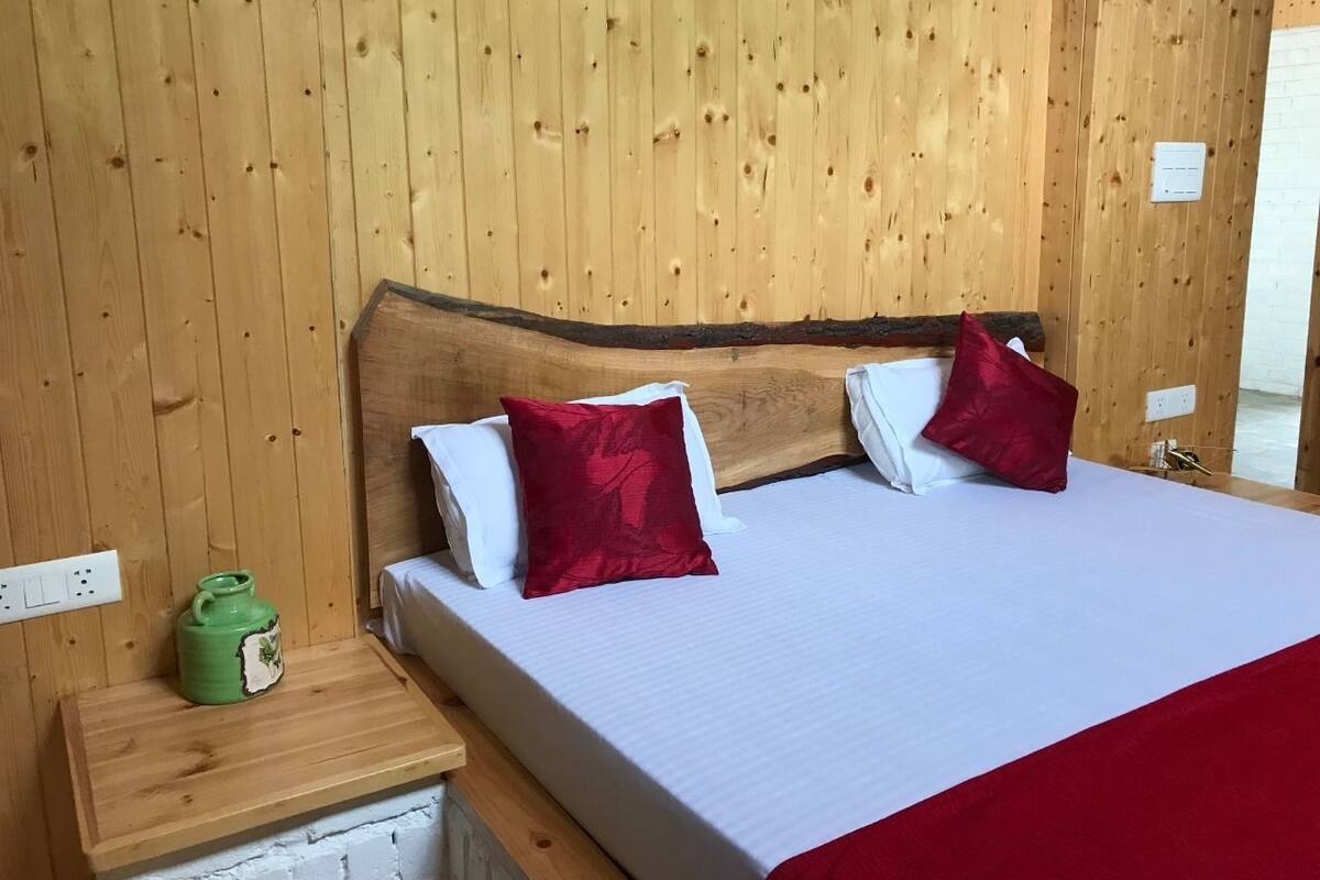 A wooden-paneled room with a bed, pillows, a nightstand, and a green ceramic jug.