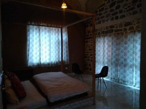 Een slaapkamer met een hemelbed, twee stoelen en een stenen muur.