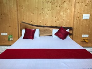 Een bed met een houten hoofdbord, witte beddengoed en rode kussens.