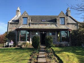 A stone building with a traditional design, featuring a central entrance, two chimneys, and a small porch with a tiled roof. - Garden Park Guest House (Grantown-on-Spey)