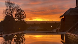Una puesta de sol tranquila sobre una piscina serena que refleja árboles y una cadena montañosa distante.