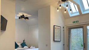Una habitación de hotel moderna con cama, una mesa de comedor con sillas, un sofá, una lámpara de techo, un cuadro enmarcado y un letrero de salida de incendios.