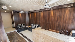 Un área de recepción con un mostrador de madera, un sofá negro con cojines estampados, un reloj y un ventilador de techo.
