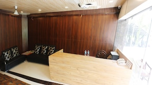 Un área de recepción moderna con un mostrador de madera, un sofá negro con cojines estampados y un ventanal que ofrece vistas al exterior.