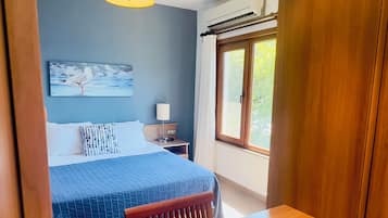 Un dormitorio con cama, mesita de noche, lámpara y una ventana con cortinas.
