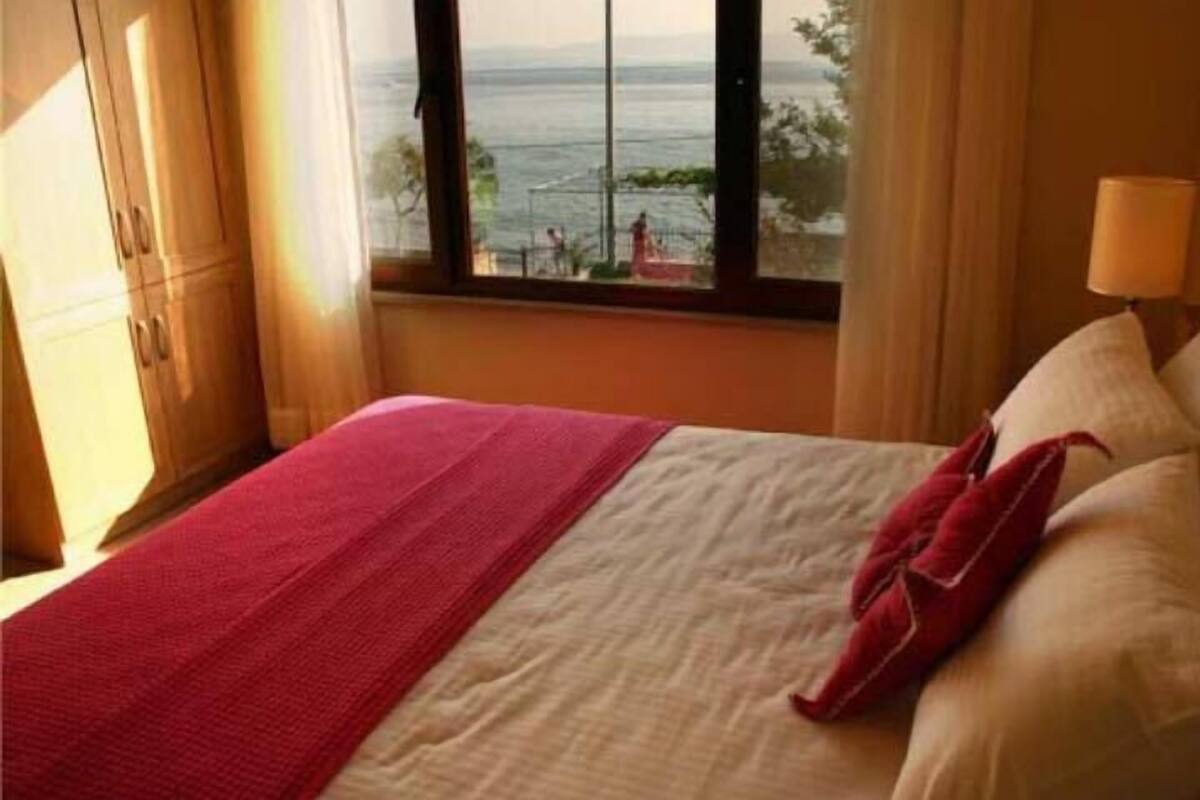 A hotel room with a bed, a window with a view of the sea, and a lamp on the nightstand.