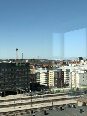 A train station with multiple tracks and platforms, surrounded by various buildings including a tall tower and a Holiday Inn sign. - City Center Tower Apartment (Tampere)