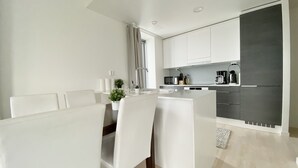A modern kitchen with white cabinets, a dining area with a white table and chairs, and a small potted plant on the counter. - City Center Tower Apartment (Tampere)