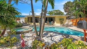Un jardin avec une piscine, des palmiers et un espace barbecue couvert.