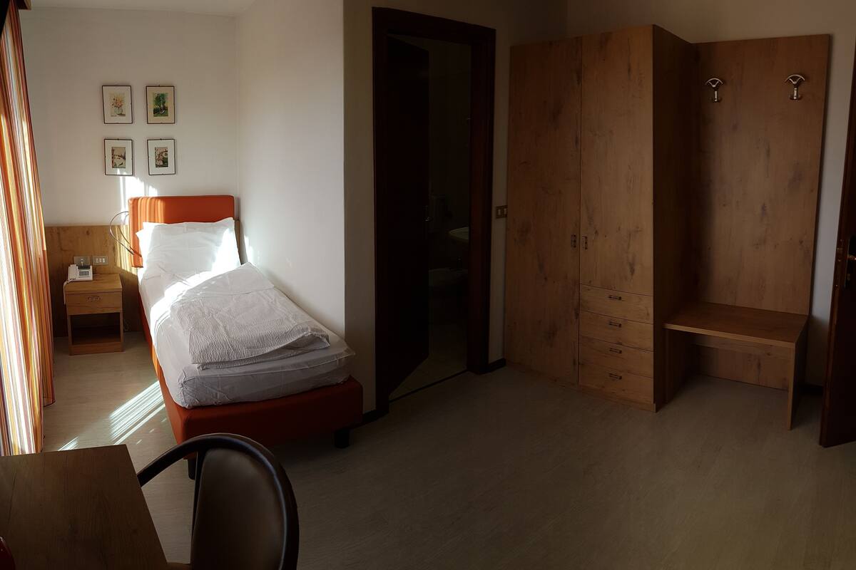 A bedroom with a bed, a wooden wardrobe, a desk, and a chair.