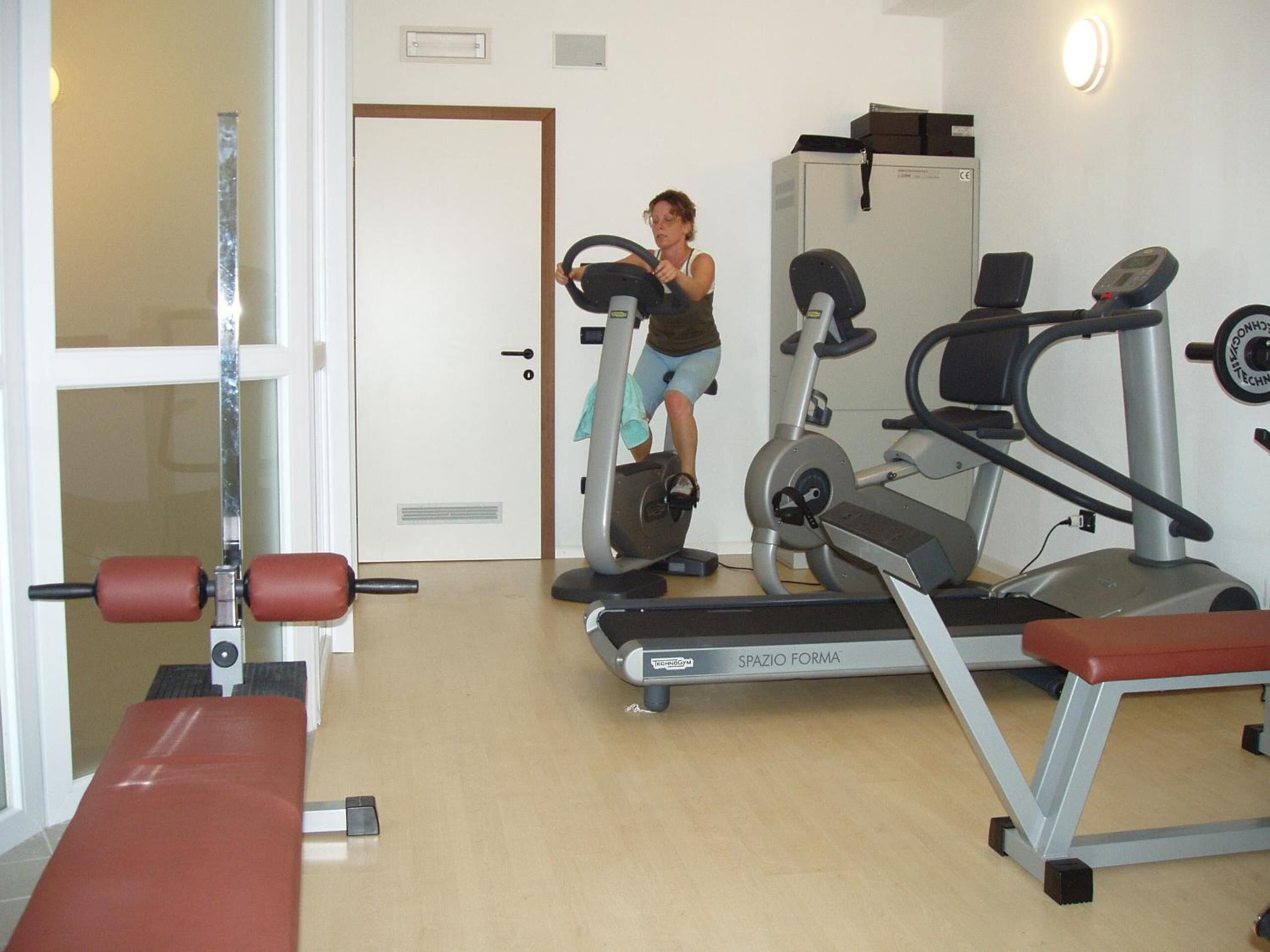 Ein Fitnessraum mit Laufbändern, einer Bank und einer Tür zu einem weiteren Raum.