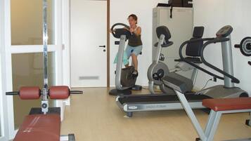 Ein Fitnessraum mit Laufbändern, einer Bank und einer Tür zu einem weiteren Raum.