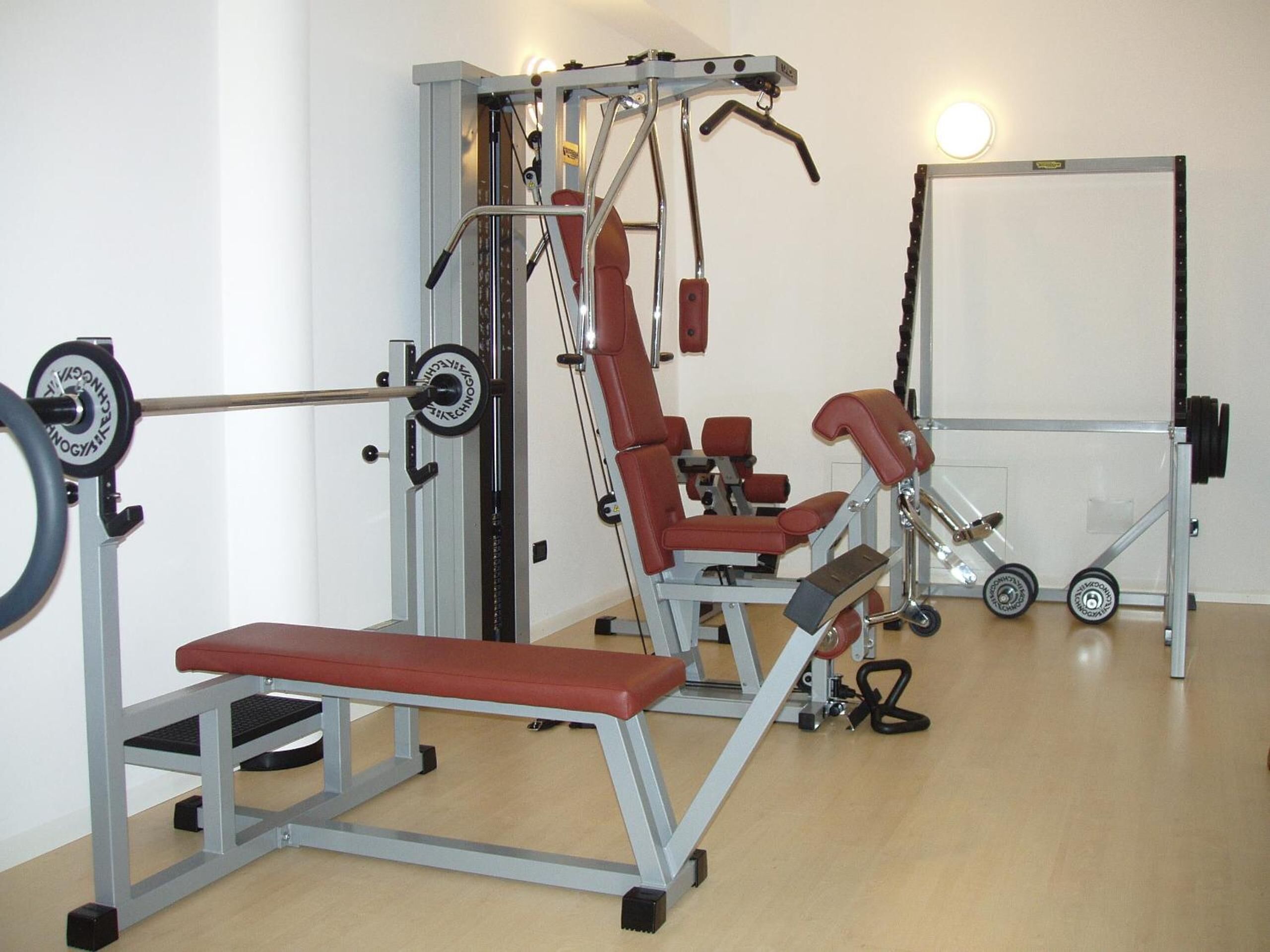 Un gimnasio con equipamiento para levantamiento de pesas, bancos y una estructura para sentadillas.